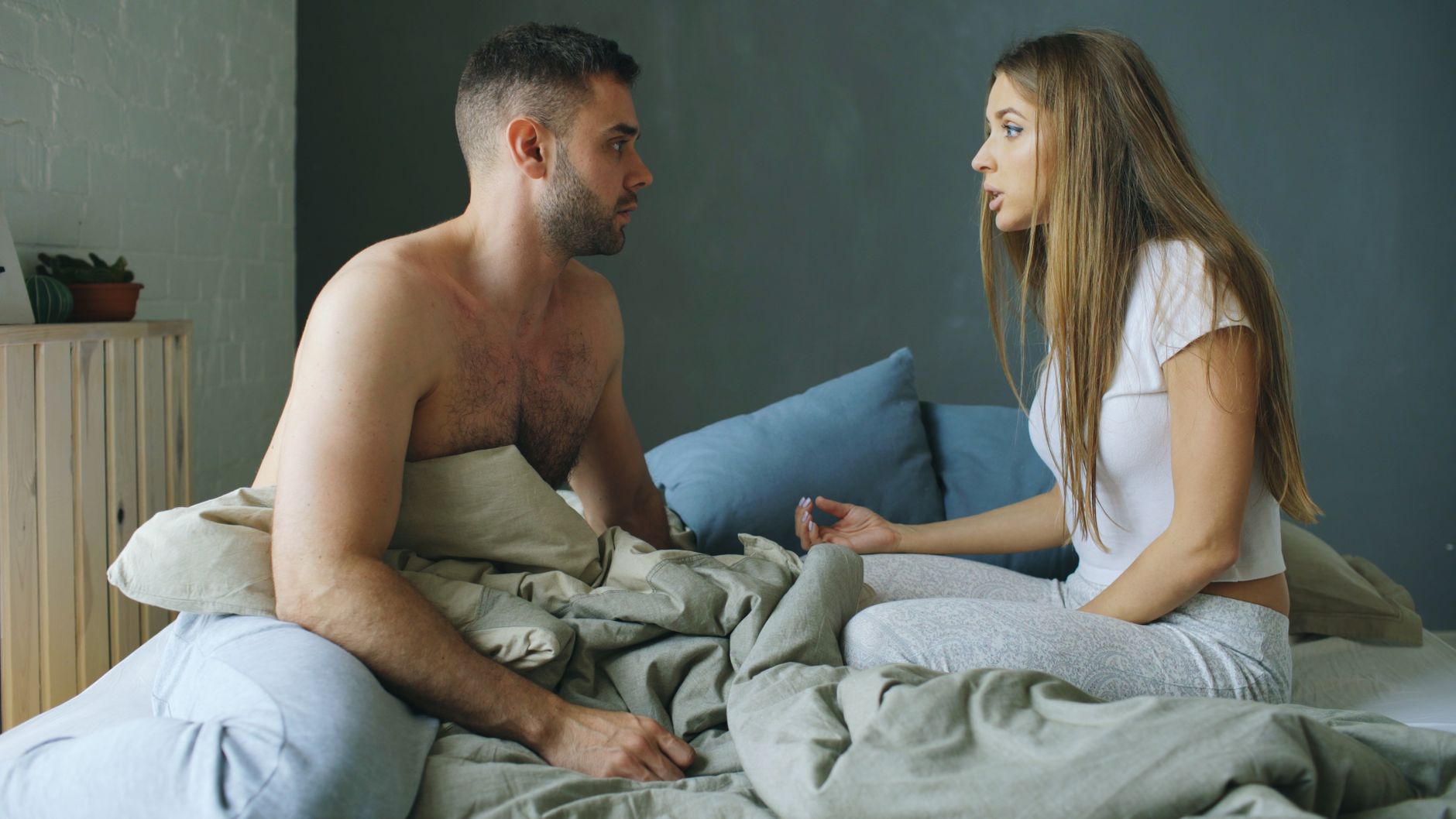 Kobieta siedzi na brzegu łóżka z ręką na podbrzuszu, a partner słucha jej ze wsparciem