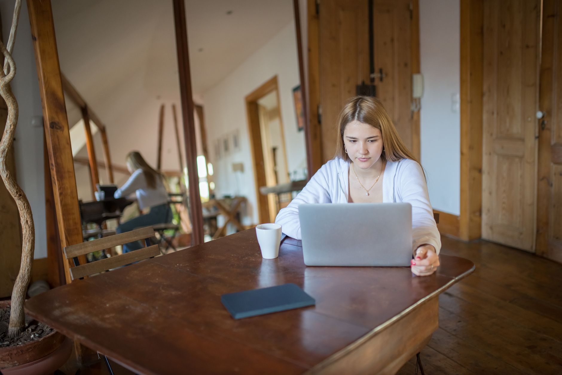 Osoba spokojnie pracuje na laptopie przy stole w domu, obok notes i kubek herbaty